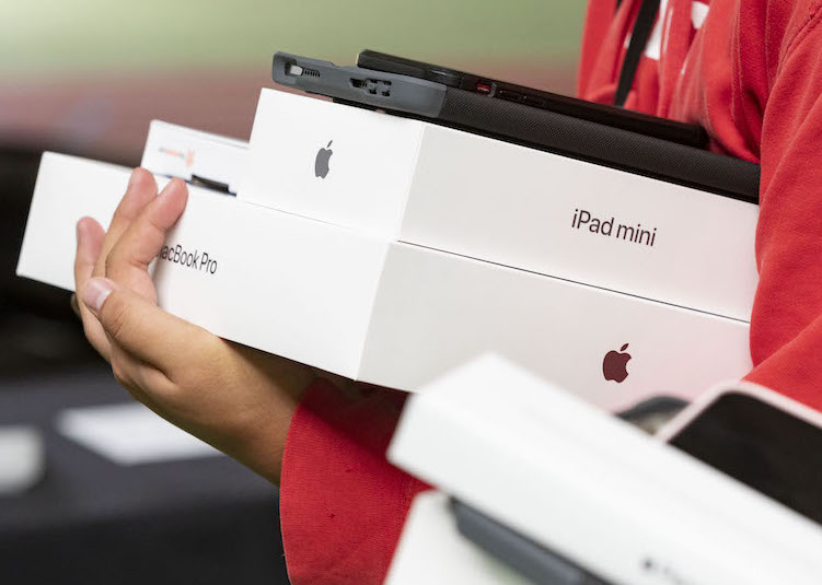 A student holding a macbook pro box and iPad mini box in a stack.