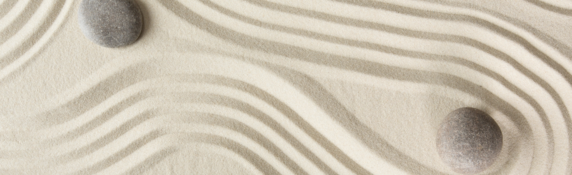 Fine sand combed in a pattern. Two smooth stones lay on top of the sand.