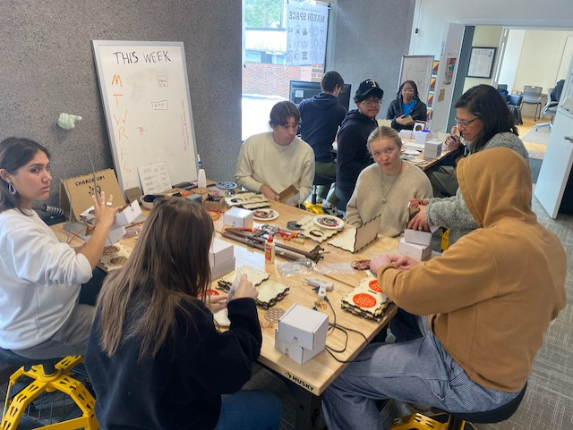A group of students around a table building their bluetooth speaker with wood pieces and wiring.