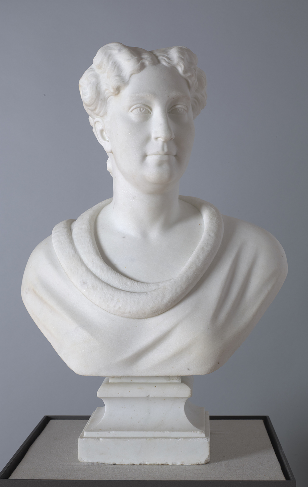Marble bust of a woman of white European descend with a middle-parted hairstyle and an open-necked blouse