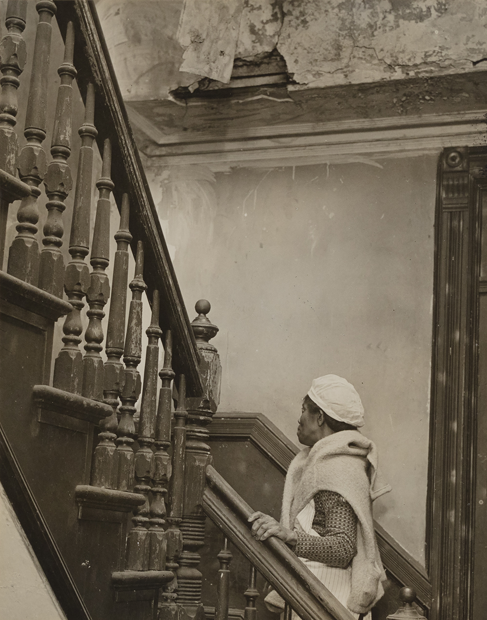 Photograph of a Black woman ascending a turned staircase in a building with crumbling architecture