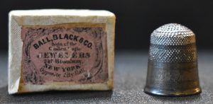 mage of a small fabric-covered box (at left) that reads: “Ball, Black and Co. Jewelers, New York,” with a used silver thimble that is engraved with the initials “P,” “A,” and “J.”