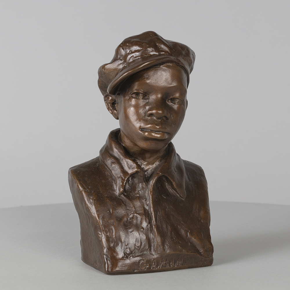 A small plaster bust painted brown of a young Black boy wearing a wrinkled shirt, slightly opened, with a bebop cap tilted to the side. The boy wears a pensive facial expression