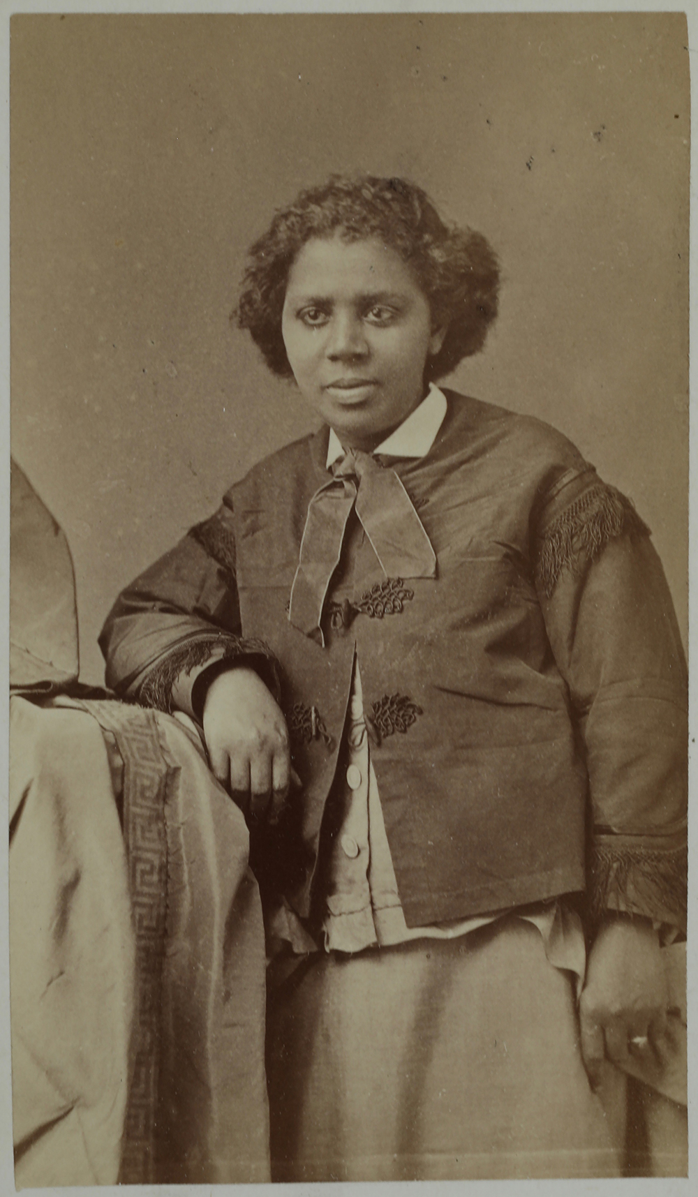 Photographic portrait of Edmonia Lewis leaning against a fabric-covered pillar and resting her proper right elbow on the pillar